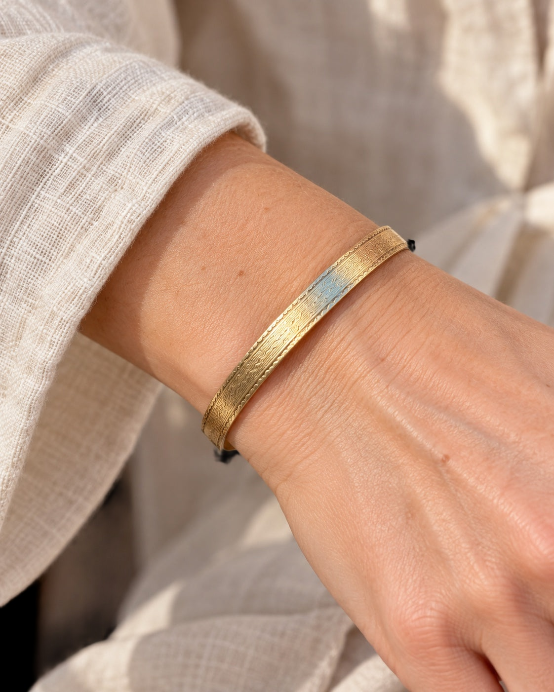 Model wearing EARLY 20TH CENTURY STEPPED WAVE 9 KARAT GOLD CASED BANGLE against a black background