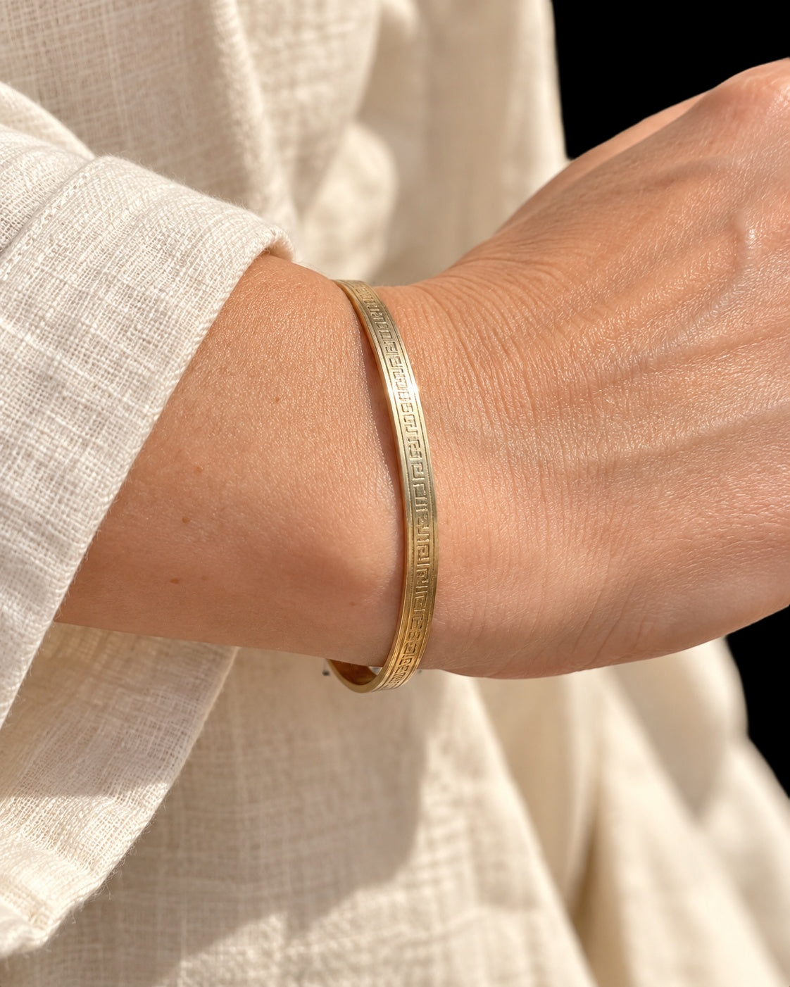 Model wearing EARLY 20TH CENTURY GREEK KEY 9 KARAT GOLD CASED BANGLE against a black background