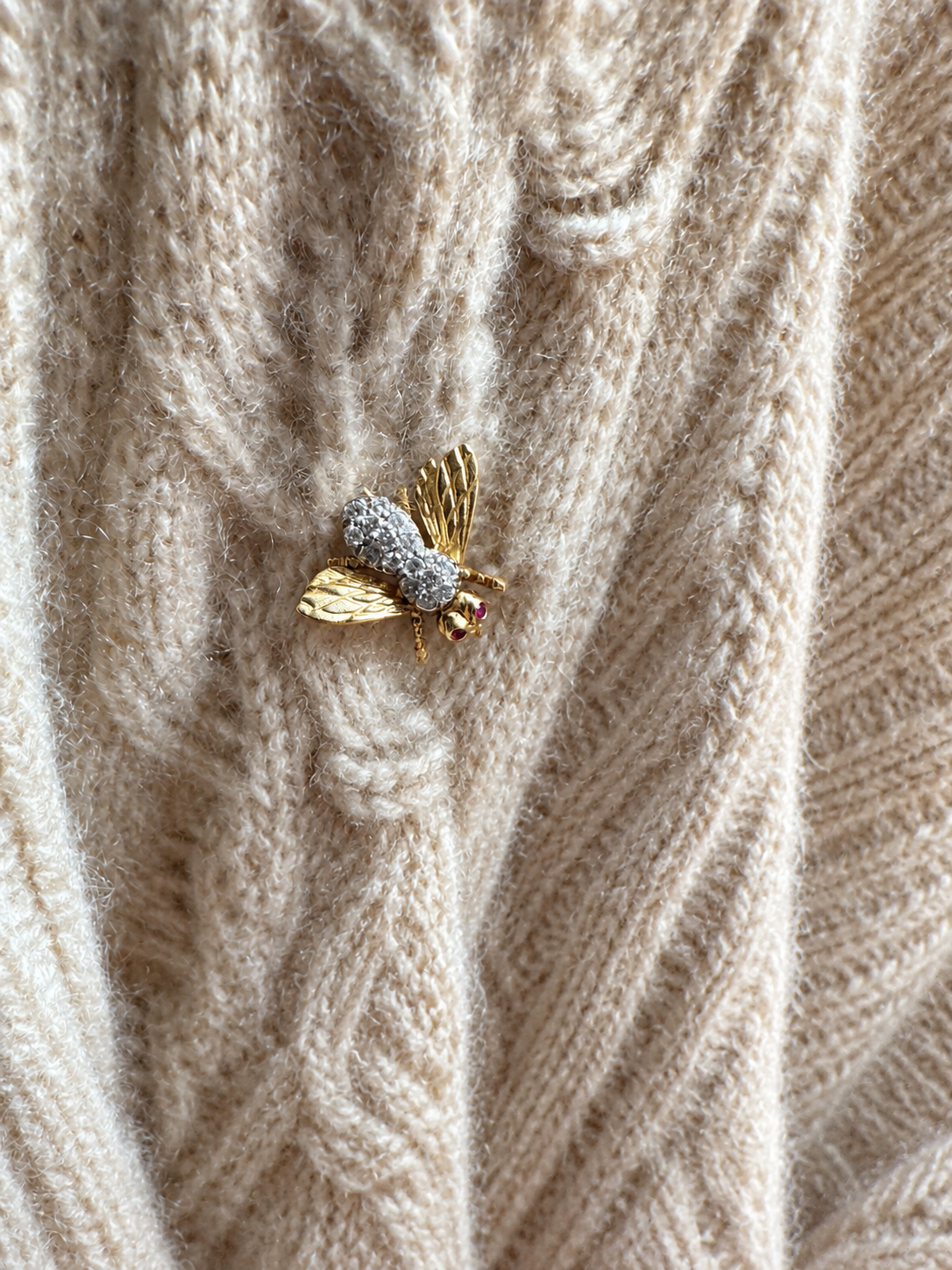 Vintage gold diamond and ruby bee brooch shown on cream cable knit cashmere