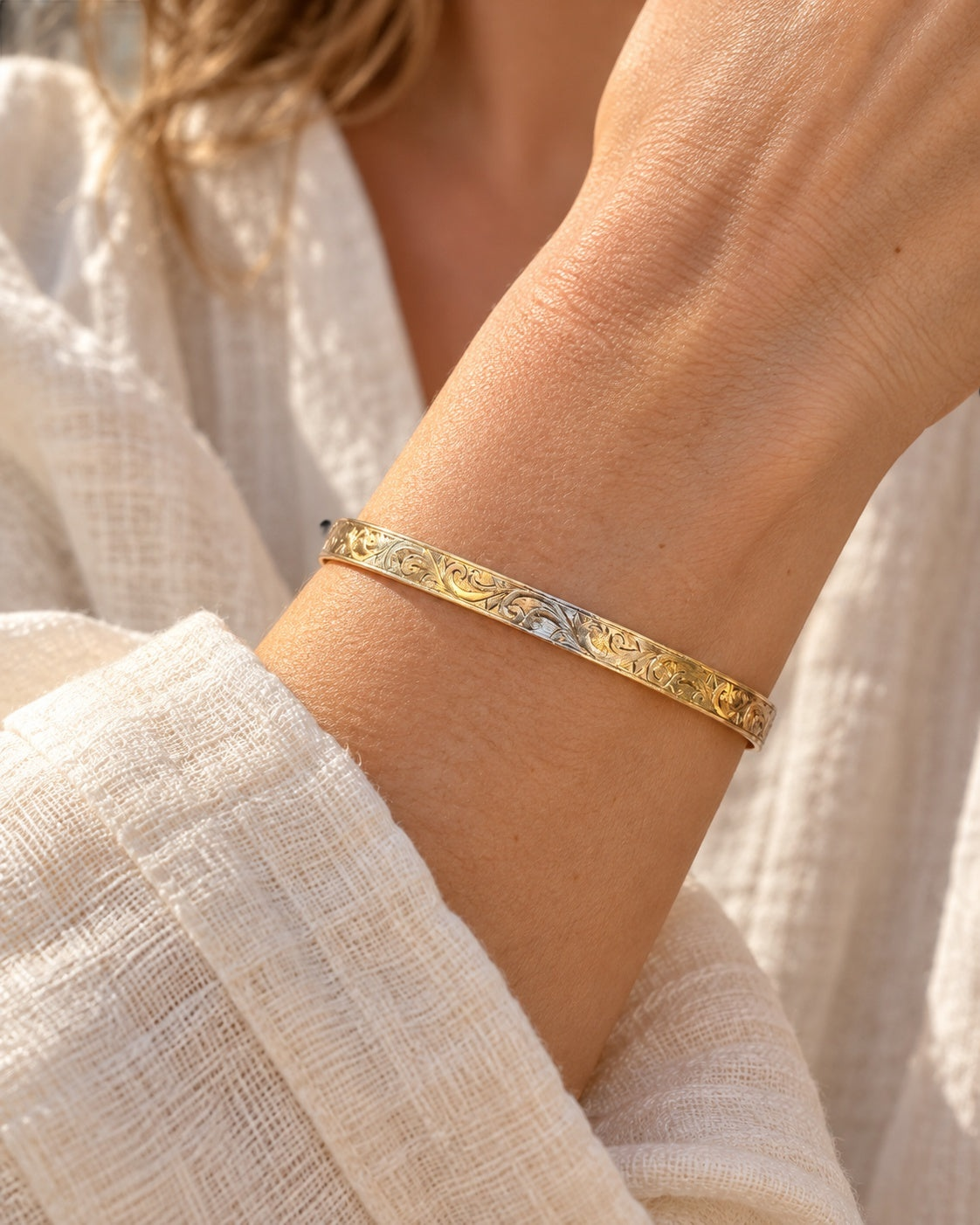 Model wearing EARLY 20TH CENTURY SCROLL 9 KARAT GOLD CASED BANGLE against a black background